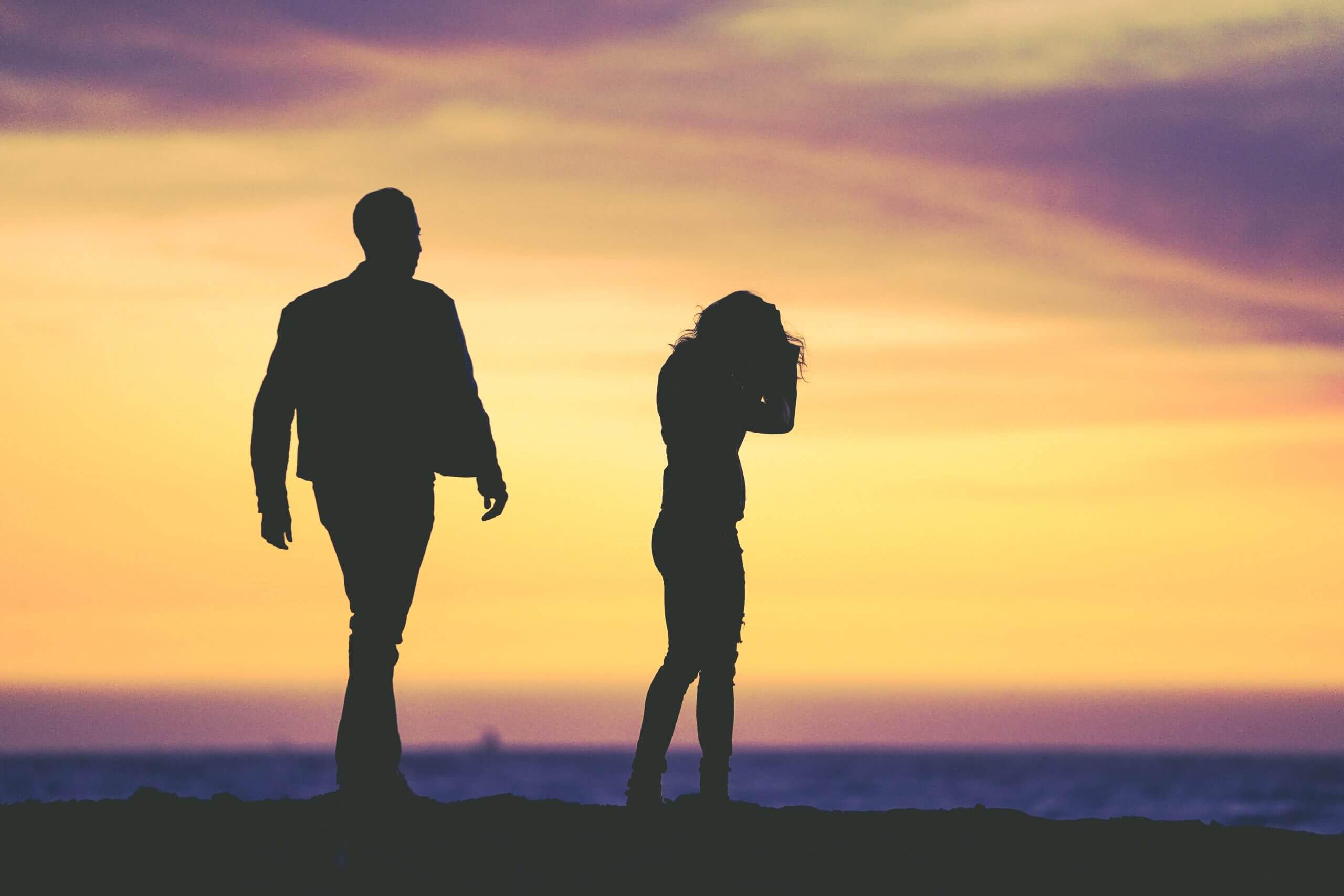 A man and woman stand together on the beach, silhouetted against a vibrant sunset sky.
