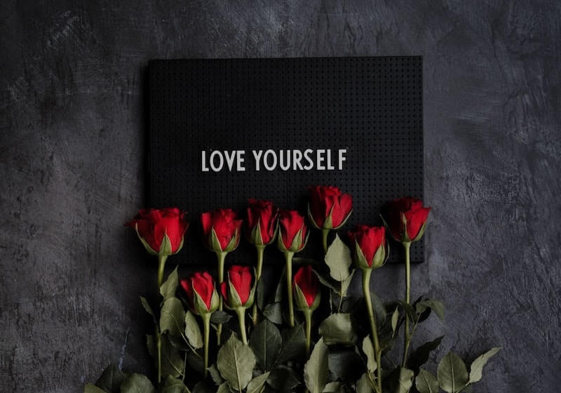 sign reading "love yourself" with red roses laid on it