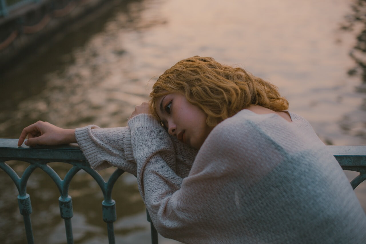 woman looking sad by the water because she's struggling with perfectionism and the pressure to be perfect