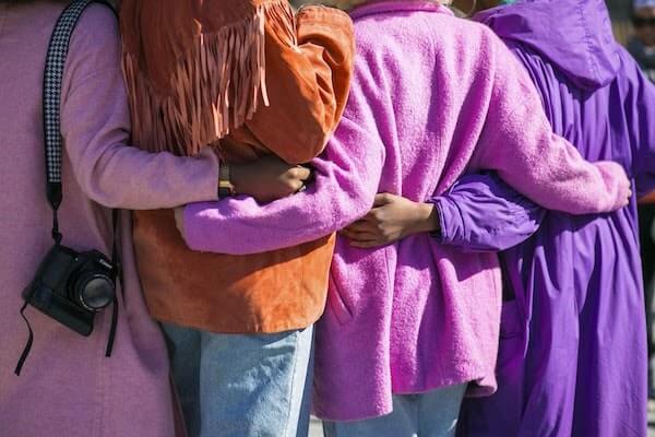 backs of a group of women wearing pink and purple coats with arms around each other