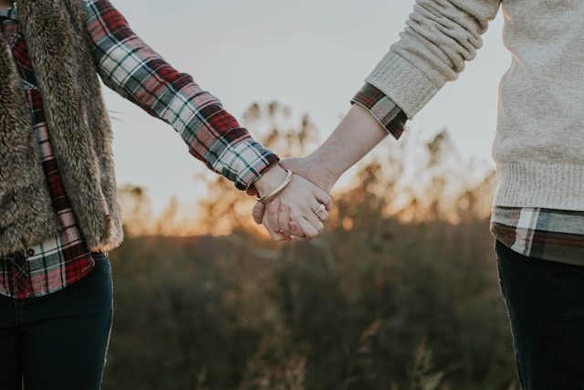 Photo of a Couple Holding Hands Slightly Apart From Each Other in a Field