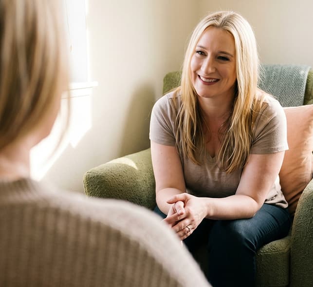 kirstin-carl seated in a chair, engaged in conversation with a therapist in a professional office setting.
