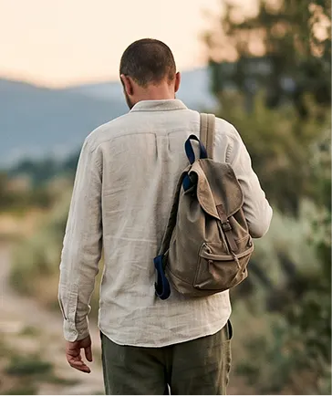 A man carrying a backpack walks along a dirt road surrounded by greenery.