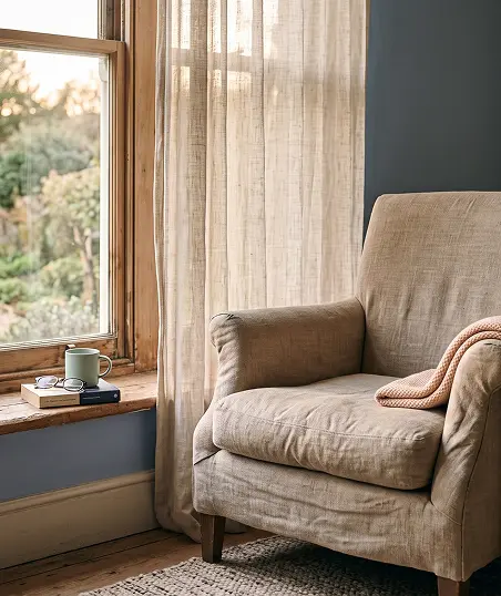 A chair positioned in front of a window, adorned with flowing curtains that frame the view outside.