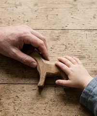 A child and an adult are smiling while holding a wooden dog toy together, showcasing a moment of playfulness.
