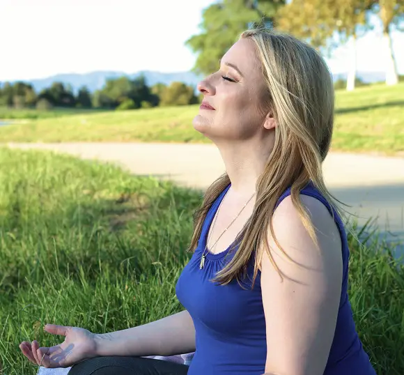 Kirstin sits cross-legged on the grass in a park